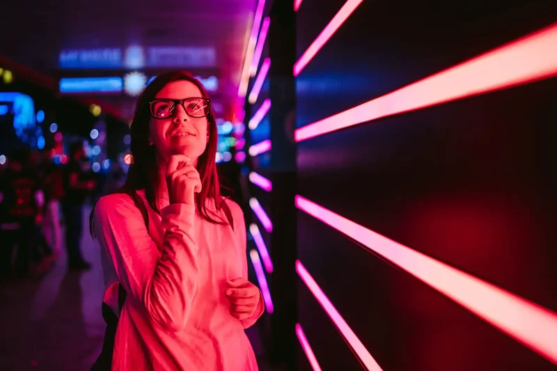 Besucherin mit Brille vor einer Lichtinstallation aus pinkfarbenen Neonröhren