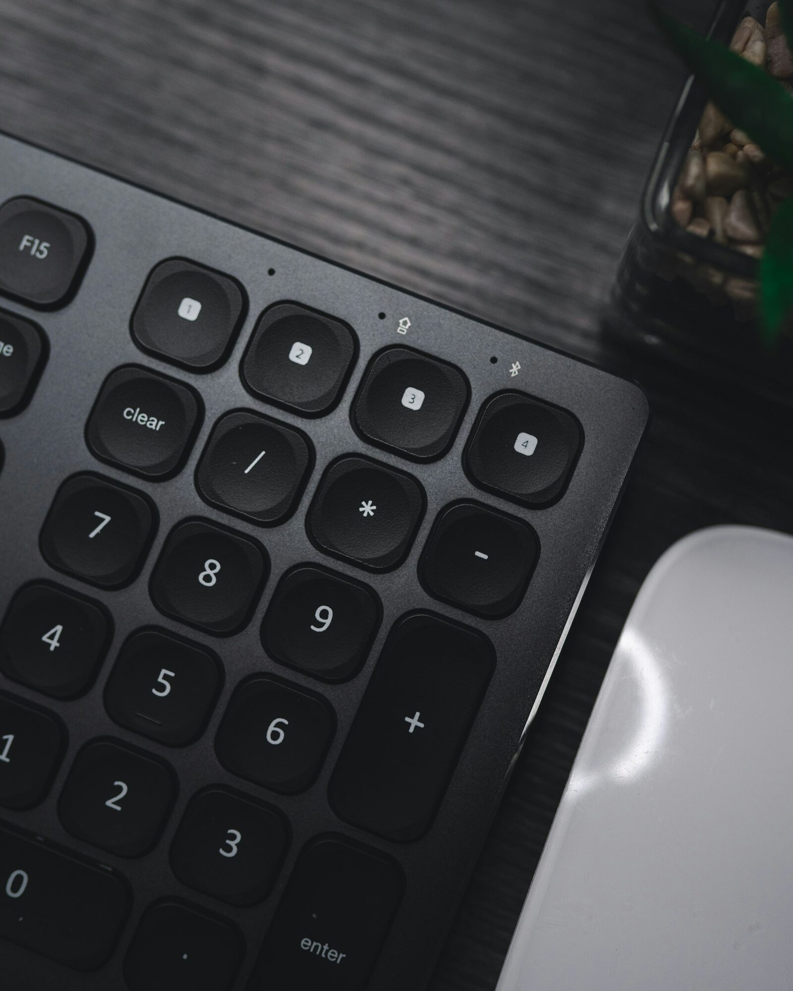 Nahaufnahme einer dunklen Tastatur mit Ziffernblock und einer weißen Maus auf einem Schreibtisch